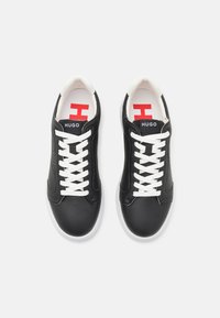 Black leather sneakers with white laces, a white rubber sole, and red Hugo logo accents on the tongue and insole. Smooth texture.