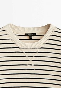 Maglione a righe con sfondo crema e righe nere, con colletto a girocollo a coste e dettagli di cucitura visibili.