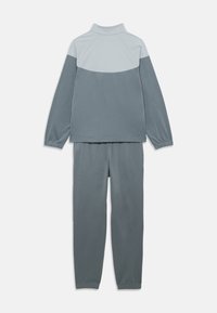 Γκρι δίχρωμο σετ φόρμας από μαλακό ύφασμα. Διαθέτει ψηλό γιακά, αντίθετο ελαφρύ γκρι πάνελ στους ώμους και ελαστικές μανσέτες στις μανίκια και το παντελόνι.