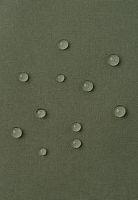 Tessuto verde texturizzato con gocce d'acqua chiare disperse sulla superficie, che mette in evidenza un design semplice e funzionale e modelli di fibra visibili.