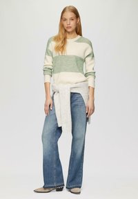 Gebreide trui in crème met groene horizontale strepen, gecombineerd met hooggesneden blauwe jeans. Lichte textuur, ontspannen pasvorm en een gestrikte grijze accent.