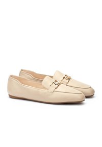Mocasines de cuero beige con suela plana, punta afilada y acento decorativo de hardware dorado en la parte frontal. Textura suave, diseño minimalista.