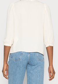 Kremfarvet bluse med puffede ærmer, lavet af glat stof, med afrundet halsudskæring og lige kant, kombineret med lyseblå denimjeans.