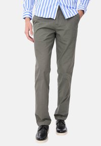 Chinos leggeri verde oliva con una vestibilità dritta, dotati di tasche laterali e una superficie in cotone morbido, abbinati a scarpe nere.
