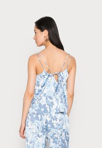 Top sem mangas de estampa floral azul clara com costa atada, alças ajustáveis e um corte solto, feito de um tecido suave e liso.