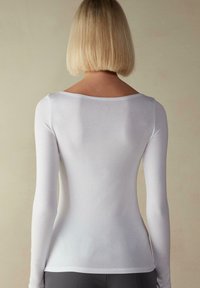 Hvid langærmet bluse med bred halsudskæring og glat tekstur. Tætsiddende design, ingen synlige mønstre og minimalistisk stil, set fra bagsiden.