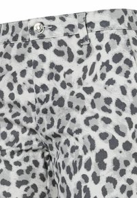 Gros plan sur un pantalon imprimé léopard gris et noir avec un bouton en métal et une boucle de ceinture à la taille.