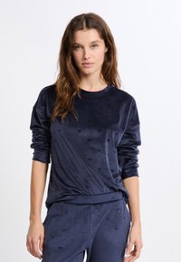 Granatowy welurowy sweter z długim rękawem, z delikatnym wzorem serc, o luźnym kroju w okolicy talii.