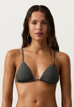 Femme aux cheveux mouillés portant un haut de bikini triangle texturé gris foncé sur un fond clair uni.