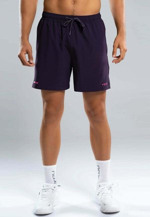 Man draagt donkerblauwe sportshort met trekkoord, witte sokken en witte sportschoenen, staand tegen een effen grijze achtergrond.