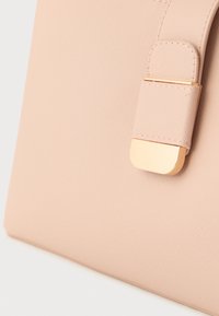 Detail ružovej kabelky s textúrovaným povrchom a zlatým obdĺžnikovým zapínaním na remienku.