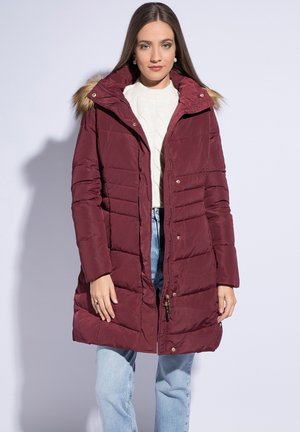 Bordeaux pufferjack met een afneembare capuchon met bontrand, ritssluiting en een doorgestikte uitstraling. Gepaard met lichtblauwe jeans.