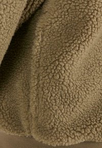 Brunt fleece-stof med en struktureret, let fuzzy overflade. Har en glat brun kant forneden.