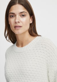Hellgrauer, gestrickter Pullover mit strukturiertem Muster, Rundhalsausschnitt und gerippten Bündchen. Das Material wirkt weich und atmungsaktiv.
