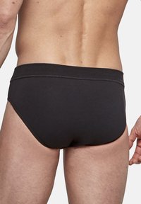 Schwarze Schwimmslips aus glattem Material mit niedrigem Bund, eng anliegendem Sitz und minimalistischem Design ohne Verzierungen.