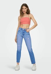 Top corto di corallo con spalline sottili, abbinato a jeans chiari strappati e sneakers bianche con suola rialzata. Design semplice e casual.