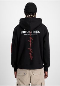 Sudadera con capucha negra hecha de una mezcla de algodón. Presenta un logo impreso en blanco, texto en rojo y un bolsillo con cremalleras en la manga izquierda.