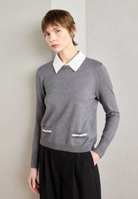 Grau melierter Pullover mit weißem Kragen, ausgestattet mit zwei vorderen Taschen mit horizontalen Reißverschlüssen. Weicher Stoff und schlanker Schnitt.