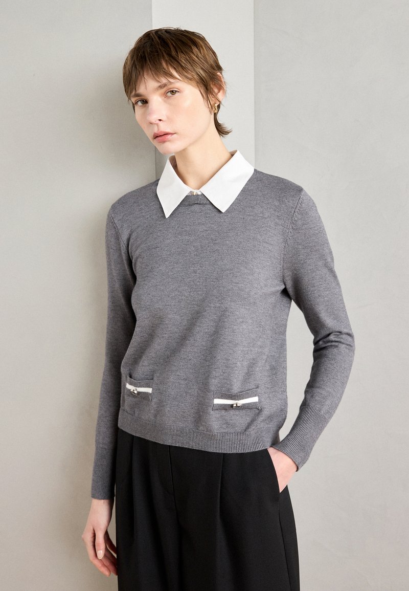 Grau melierter Pullover mit weißem Kragen, ausgestattet mit zwei vorderen Taschen mit horizontalen Reißverschlüssen. Weicher Stoff und schlanker Schnitt.
