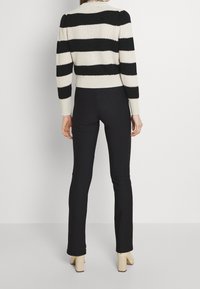 Pull en tricot à rayures noires et crème avec un design court, associé à un pantalon noir ajusté et des chaussures à talons carrés de couleur claire.
