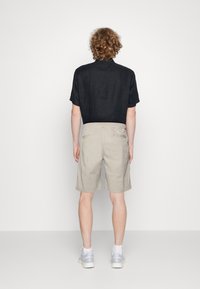 Black short-sleeved linen shirt, beige shorts with back pockets, light grey athletic shoes, presented from the back against a plain background.