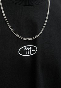 Zwarte sweatshirt met een wit ovale logo met drie palmboompjes, vergezeld van een zilveren ketting. Zachte stofstructuur.