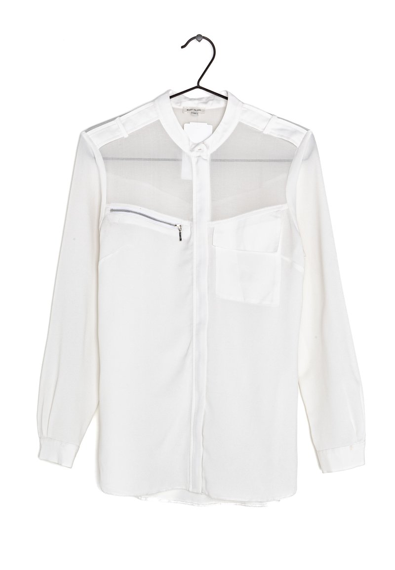 Blouse blanche à manches longues avec une section supérieure transparente, fermeture à boutons et deux poches, dont une avec une fermeture éclair. Texture de tissu lisse.