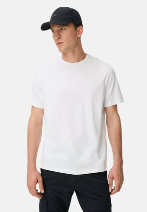 Weißes Baumwoll-T-Shirt mit kurzen Ärmeln, Rundhalsausschnitt und dezentem Logo auf der Brust. Kombiniert mit einer marineblauen Baseballkappe.
