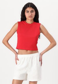 Rød, kortermet topp uten ermer laget av glat stoff, kombinert med hvite shorts med blomstermønster i øyelet og elastisk midjebånd.