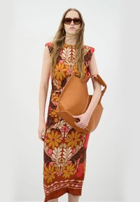 Flydende brun blomstret mønstret kjole med tætsiddende silhuet; tan læder tote bag med struktureret form og kontrasterende syninger. Brune solbriller.