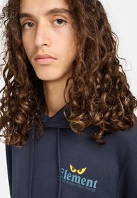 Marinblauer Kapuzenpullover mit einem grafischen Design, das das Wort "Element" und ein gelbäugiges Emblem auf der Brust zeigt. Weicher, strukturierten Stoff.