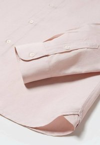 Camisa rosa claro abotonada, con un cuello estructurado y puños arrollados, que presenta botones blancos y una textura de tela suave.