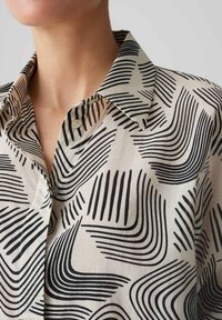 Camicia in tessuto leggero con un motivo lineare nero. Presenta un colletto classico e bottoni, mostrando una texture liscia e un design strutturato.
