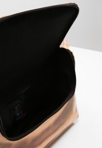 Borsa sintetica color oro rosa con chiusura a zip, dotata di una foderatura interna nera e una piccola tasca interna. Texture liscia, forma rettangolare.