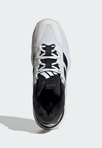 Chaussure de sport blanche et noire avec une tige en maille, des lacets plats et un col rembourré. Présente trois rayures noires sur le côté. Design à bout rond.