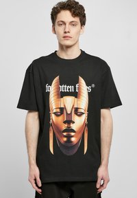 Camiseta de algodón negra con un gran gráfico de una máscara dorada, con detalles elaborados, y el texto "objetos olvidados" en blanco encima del diseño.