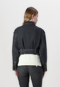 Svart denimjakke med en cropped design, som har et belte i midjen, glidelåser på ermene, og en jevn tekstur.