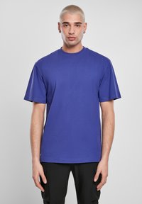 Kameros, trumpomis rankovėmis marškinėliai ryškiai violetinės spalvos. Klasikinis apvalus iškirpimas, laisvas siluetas, lygi tekstūra, minimalus dizainas.