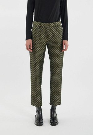Pantalons verts à motifs géométriques, fabriqués dans un tissu à la texture lisse. Coupe droite, portés avec des bottines noires.