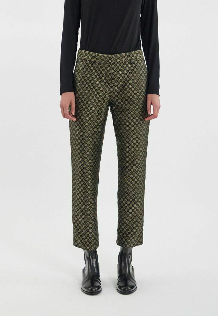 Pantalons verts à motifs géométriques, fabriqués dans un tissu à la texture lisse. Coupe droite, portés avec des bottines noires.