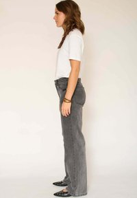 Jean gris taille haute avec une coupe droite, assorti à un t-shirt blanc uni et des ballerines noires pointues. Design simple avec des détails minimaux.