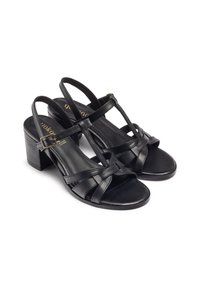 Black leather heeled sandals featuring crisscross straps, a cushioned footbed, and a block heel. Adjustable ankle strap with metal buckle.