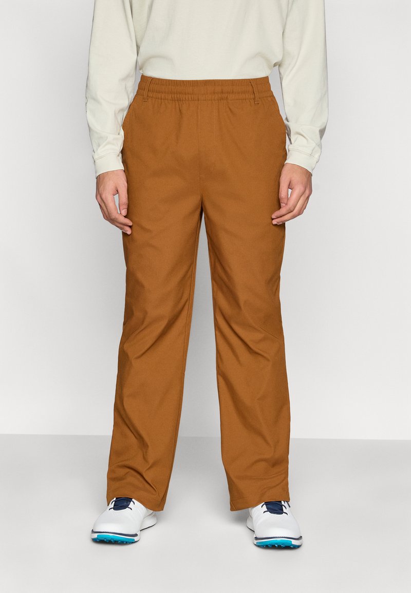 Pantalon marron à jambes droites avec une taille élastique. Fabriqué dans un tissu lisse et léger. Porté avec un haut crème à manches longues.