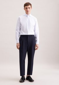 Koszula w białe i jasnoniebieskie paski z ostrym kołnierzykiem, zestawiona z granatowymi plisowanymi spodniami i czarnymi sznurowanymi butami.