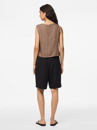 Brunrandig ärmlös topp med lös passform, kombinerad med svarta shorts. Platta sandaler fulländar outfiten, mot en neutral bakgrund.