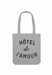 Sac fourre-tout en tissu gris avec deux poignées. Texte noir "HÔTEL de l'amour" imprimé en évidence sur le devant. Forme rectangulaire simple.