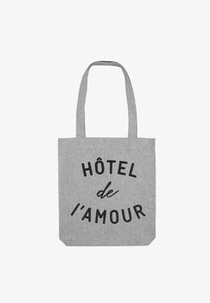 Grijze stoffen draagtas met twee schouderbanden. Zwarte tekst "HÔTEL de l'amour" prominent op de voorkant gedrukt. Eenvoudige rechthoekige vorm.