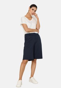 Navy blue tailored shorts with a flat front, featuring a smooth, lightweight fabric. Paired with a white, short-sleeved, relaxed-fit top.
