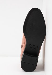 Růžová semišová bota s kulatou špičkou a texturovanou černou gumovou podrážkou. Obsahuje vyšívaný design a malé logo na podrážce.