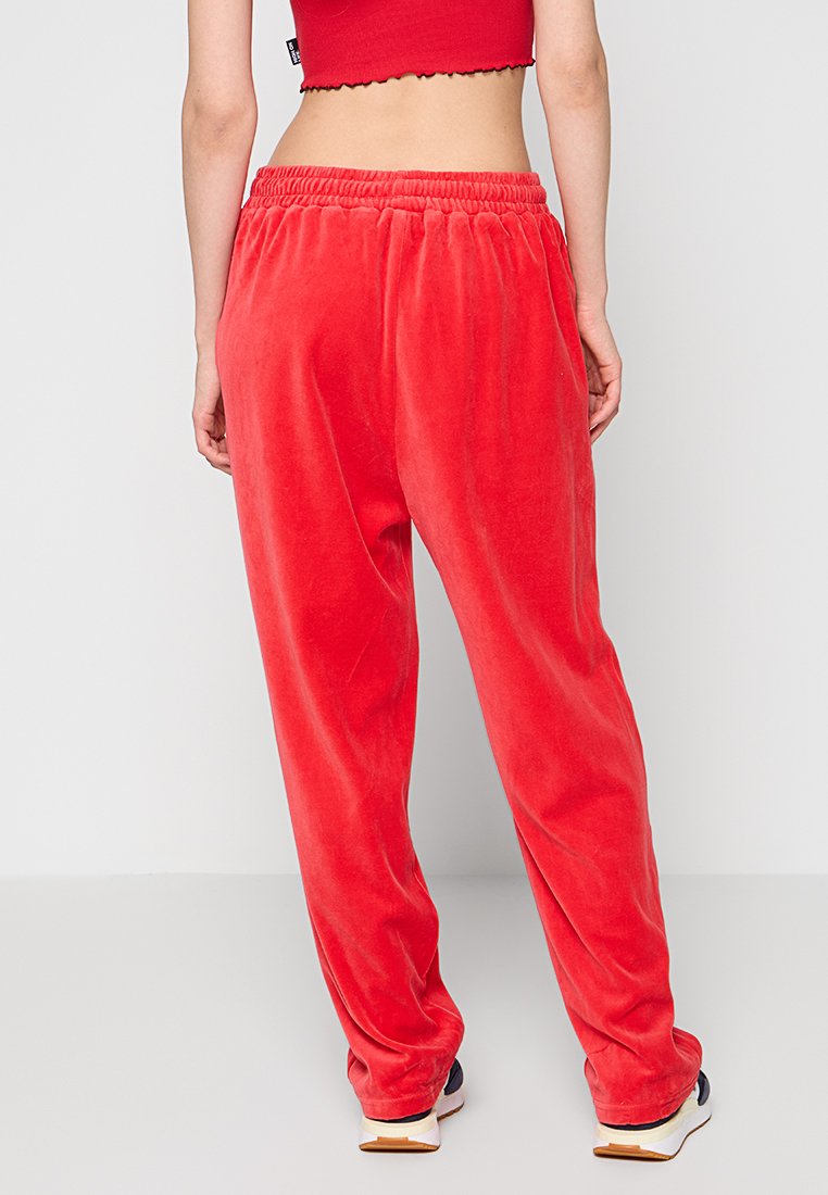 Rote Samt-Sweatpants in lockerer Passform mit elastischem Bund. Glatte Textur, keine sichtbaren Muster, kombiniert mit weißen und marineblauen Sneakers.